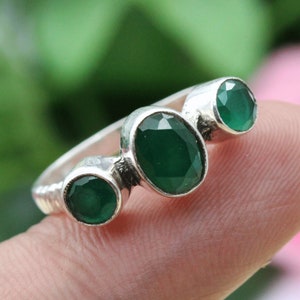 Op de afbeelding: Een zilveren ring met drie ovale groene edelstenen. De ring wordt gedragen aan een vinger.