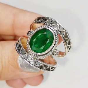 Könnte beinhalten: Ein silberner Ring mit einem ovalen, smaragdgrünen Edelstein, der in einer silbernen Fassung sitzt. Der Ring hat ein dekoratives, filigranes Design mit einem verdrehten Band.