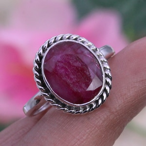 May include: A silver ring with a red oval gemstone set in a rope-like border.