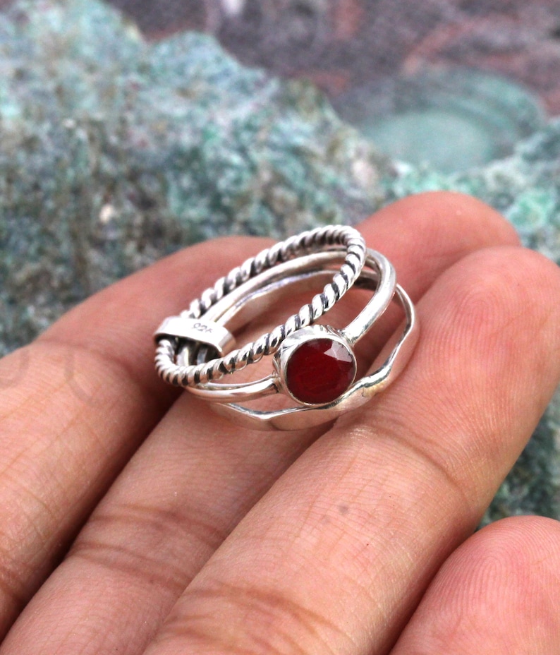 May include: A silver ring set with three bands, one of which is twisted. The top band features a red gemstone.