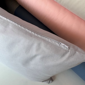 May include: A light gray pillow with a zipper closure. The pillow is made of a soft, textured fabric.