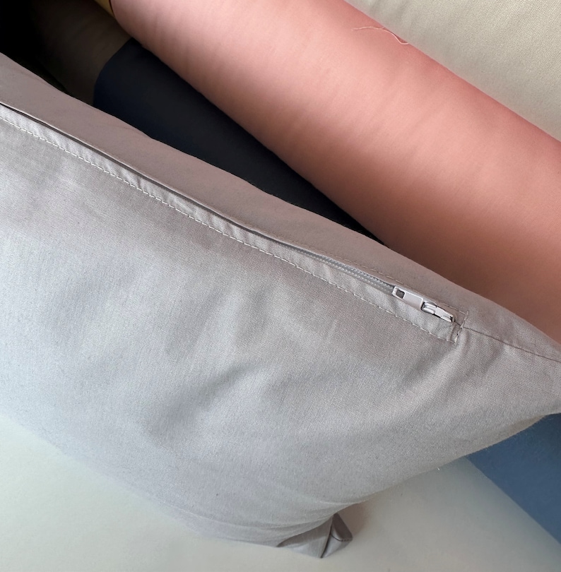 May include: A light gray pillow with a zipper closure. The pillow is made of a soft, textured fabric.