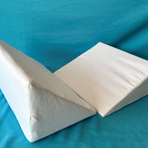 May include: Two white triangular foam wedges, possibly for sleeping or elevating legs, on a turquoise blue background.