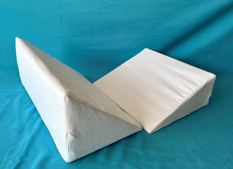 May include: Two white triangular foam wedges, possibly for sleeping or elevating legs, on a turquoise blue background.