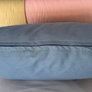 May include: A gray pillow with a zipper closure. The zipper is visible and is made of a dark blue material.
