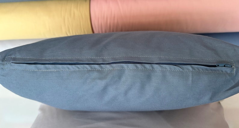 May include: A gray pillow with a zipper closure. The zipper is visible and is made of a dark blue material.