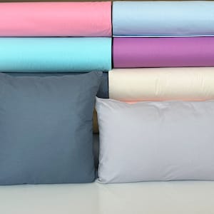 May include: Two pillows, one gray and one light gray, are in front of a stack of fabric rolls in various colors, including pink, light blue, purple, cream, yellow, and light blue.