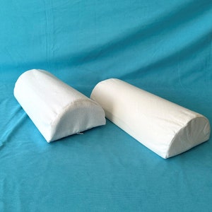 May include: Two white, cylindrical pillows with rounded ends. The pillows are made of a soft, white fabric and are lying on a blue surface.