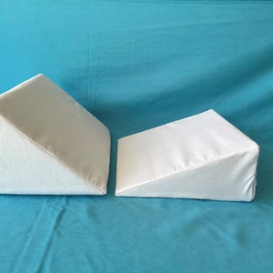 May include: Two white triangular pillows on a turquoise blue surface. The pillows are made of a soft, white fabric and are designed to provide support and comfort.