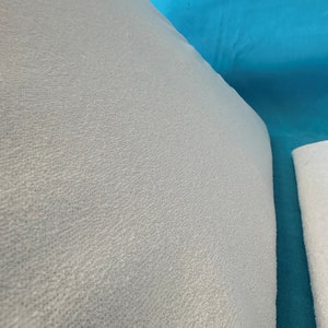 May include: Close-up of a light gray, textured fabric. The fabric has a soft, fuzzy appearance.