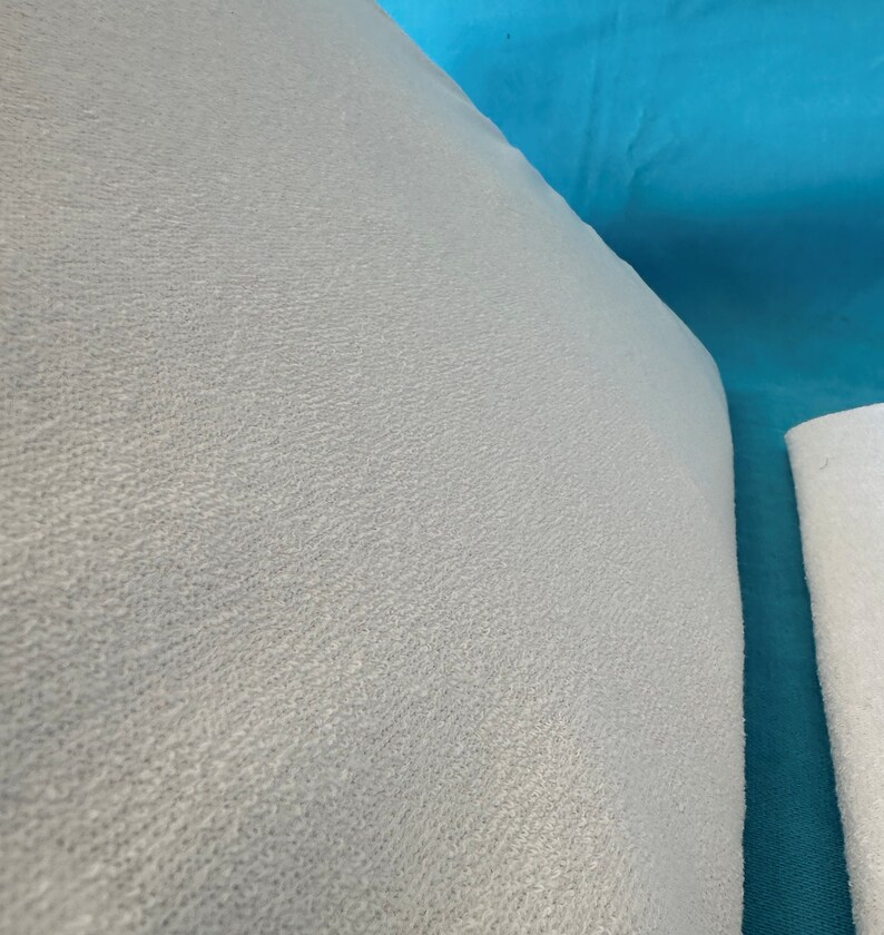 May include: Close-up of a light gray, textured fabric. The fabric has a soft, fuzzy appearance.