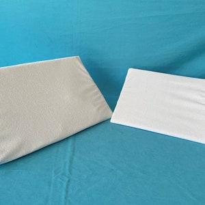 May include: Two white wedge pillows, one larger than the other, on a blue background.
