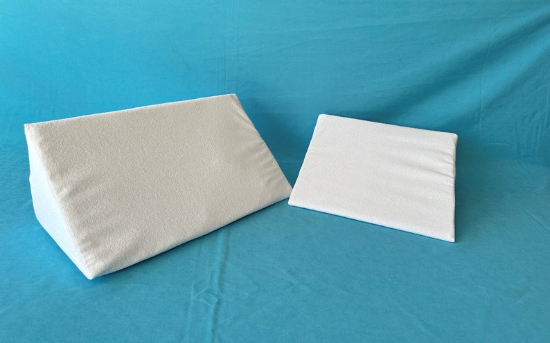 May include: Two white wedge pillows, one larger than the other, on a blue background.