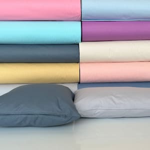 May include: A stack of fabric rolls in various colors, including pink, blue, yellow, and cream. Two pillows are in the foreground, one is gray and the other is light gray.