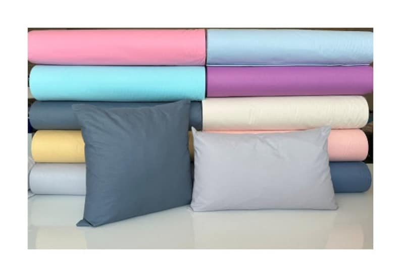May include: A stack of fabric rolls in various colors, including pink, blue, purple, cream, and yellow. Two pillows are in front of the fabric rolls, one is dark blue and the other is light gray.