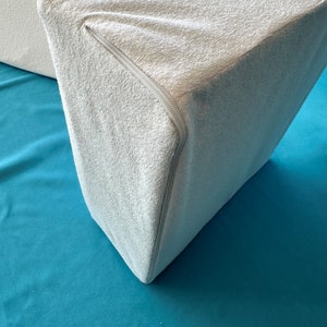 May include: A white wedge pillow with a zippered cover. The pillow is made of a soft, plush material and is designed to provide support and comfort.