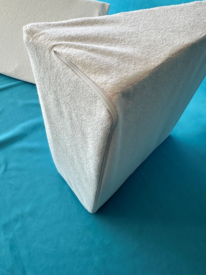May include: A white wedge pillow with a zippered cover. The pillow is made of a soft, plush material and is designed to provide support and comfort.