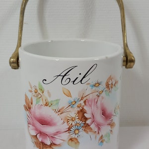 Peut inclure: Pot en céramique blanche avec une anse en laiton. Le pot est décoré d'un motif floral avec des roses roses et une inscription noire qui dit "Ail".
