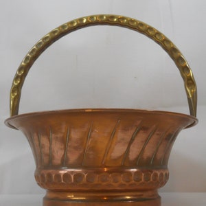 May include: A copper planter with a brass handle. The planter has a hammered finish and a fluted design.