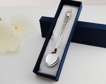 May include: A silver baby spoon with an ornate design, presented in a blue velvet gift box.
