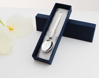 May include: A silver spoon in a blue velvet box. The spoon has a simple design and a rounded bowl.