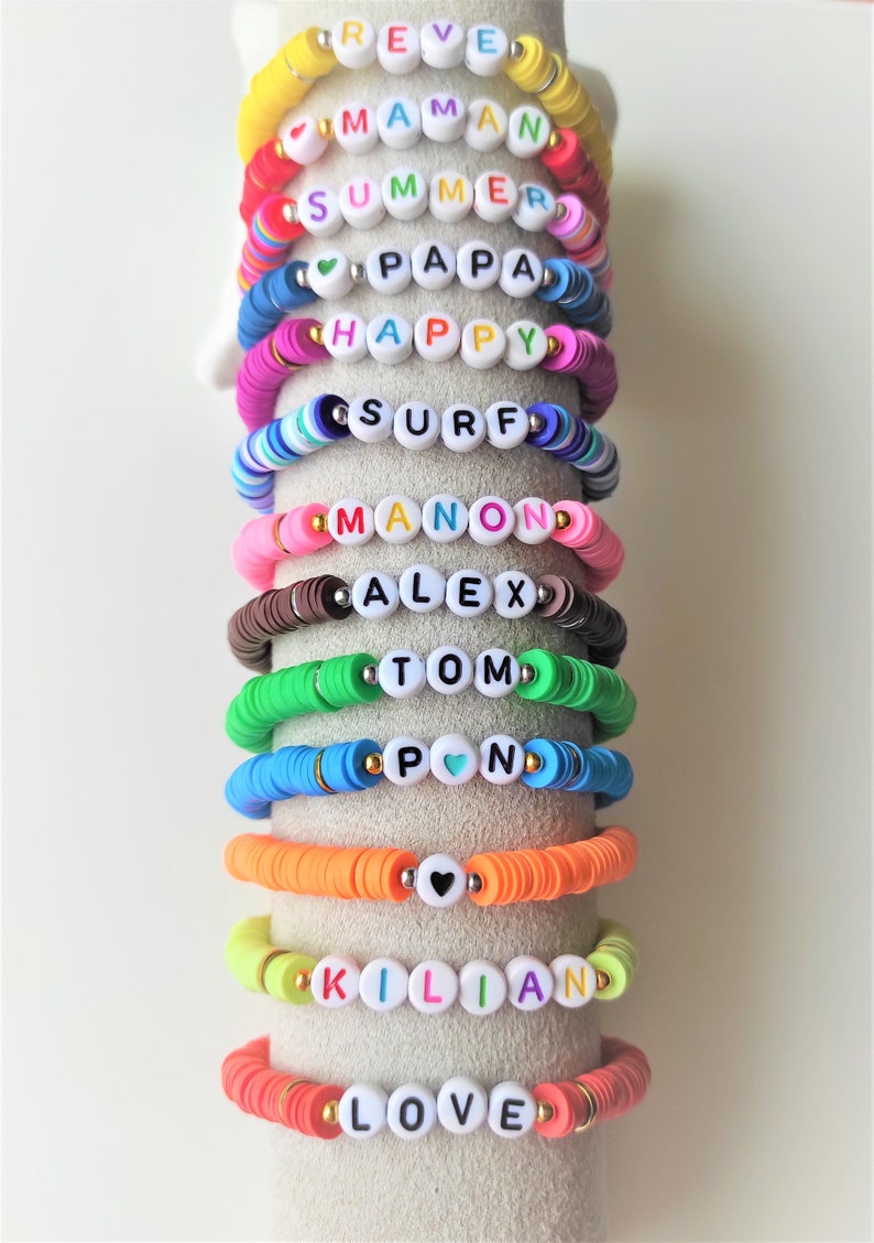 May include: A collection of colorful beaded bracelets with white letter beads spelling out words and names like "SUMMER", "HAPPY", and "LOVE". The bracelets are in various colors, including yellow, pink, blue, and orange.