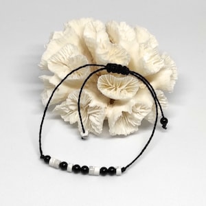 Peut inclure: Un bracelet en perles noires et blanches avec un cordon noir et une fermeture à nœud coulissant réglable.