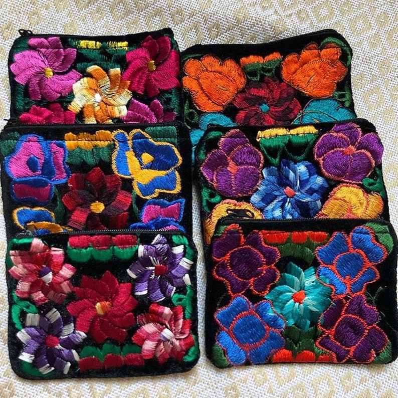 May include: Six small black velvet zippered pouches with colorful embroidered floral designs. The pouches are arranged in two rows of three. The flowers are in shades of pink, purple, blue, yellow, and orange.