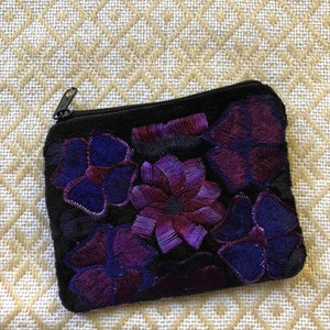 May include: A small black velvet coin purse with a zipper closure. The purse is decorated with embroidered purple and blue flowers.
