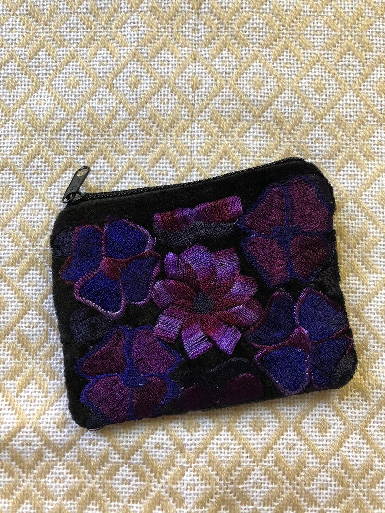 May include: A small black velvet coin purse with a zipper closure. The purse is decorated with embroidered purple and blue flowers.