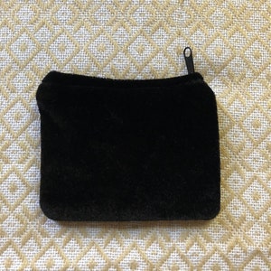 May include: A black velvet zippered pouch. The pouch is lying flat on a white and gold patterned fabric.