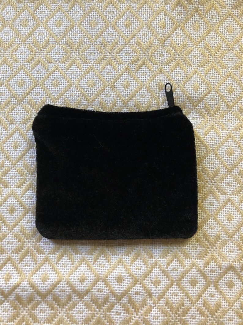 May include: A black velvet zippered pouch. The pouch is lying flat on a white and gold patterned fabric.