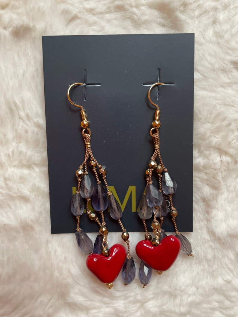 May include: A pair of dangle earrings with red heart charms. The earrings feature a gold chain with purple glass beads.