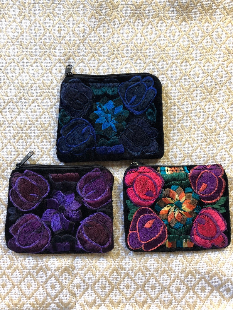 May include: Three small zippered pouches with embroidered floral designs. The pouches are black with purple, blue, and pink flowers.