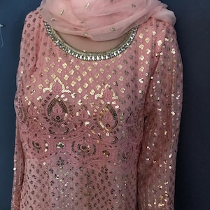 May include: A pink and gold sequined dress with a matching pink dupatta. The dress has a round neckline and long sleeves. The dupatta is sheer and has a delicate floral pattern.
