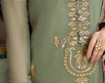 May include: Sage green embroidered tunic with gold accents. The tunic features intricate gold embroidery along the neckline, sleeves, and bodice. The long sleeves are sheer, and the garment is adorned with decorative buttons and a detailed floral design.