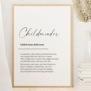 May include: A framed print with the word "Childminder" in elegant script. The definition below describes a caregiver's role, emphasizing care, comfort, and joy. The print is in a light wood frame, with a vase of dried flowers and a stack of books in the background.