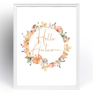 May include: A framed print with a watercolour floral wreath. The wreath includes pumpkins and leaves in orange, yellow, and green. The words "Hello Autumn" are written in a cursive font inside a white circle.