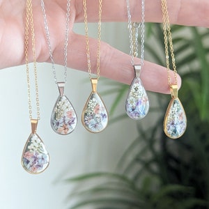 May include: Five gold and silver necklaces with teardrop-shaped pendants filled with pressed flowers. The pendants are clear and show the flowers in detail.