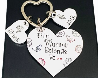 May include: A silver heart-shaped keyring with the text "This Mummy Belongs To" and a floral design. There are two smaller heart-shaped charms attached to the keyring with the names "Mavis" and "Jack" on them.