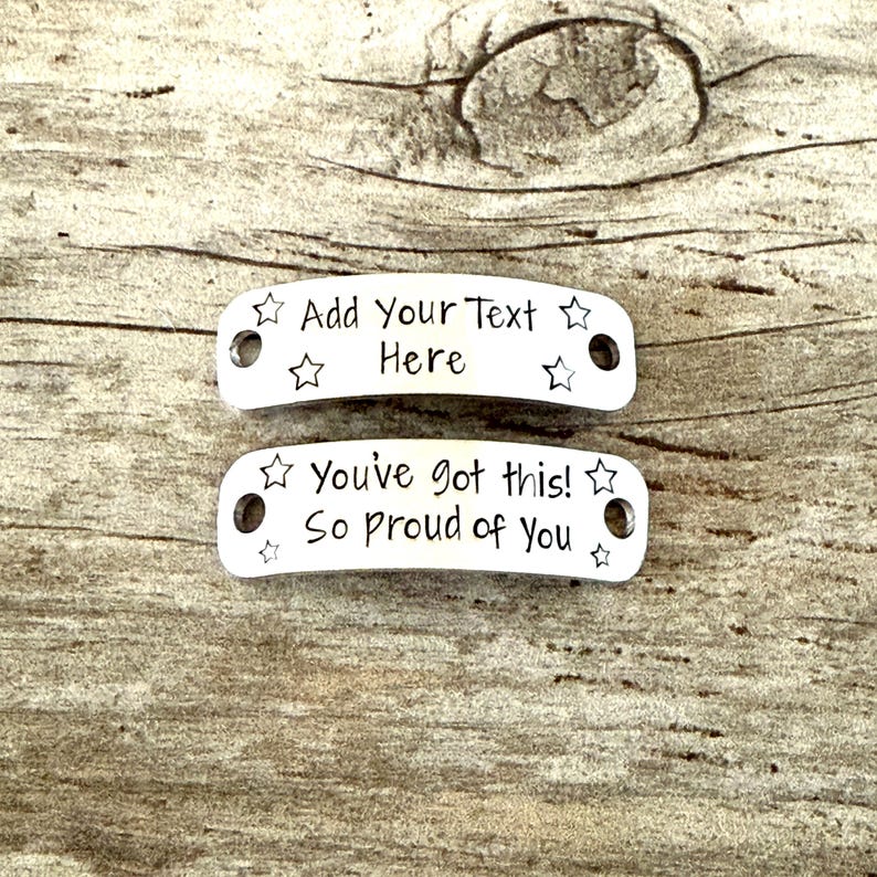 May include: Two silver metal tags with rounded edges and star accents. The top tag reads "Add Your Text Here." The bottom tag says "You've got this! So proud of You." Both tags have holes for attaching.