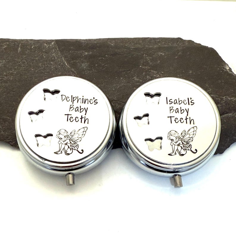 Puede incluir: Dos cajas plateadas para guardar dientes de beb&eacute;. Cada tapa de la caja tiene las palabras "Delphine's Baby Teeth" e "Isabel's Baby Teeth" impresas. Las tapas tambi&eacute;n presentan ilustraciones de dientes y hadas.