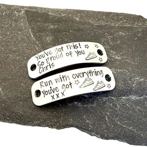 May include: Two silver-colored shoe tags with engraved text and running shoe illustrations. One tag reads "You've got this! So proud of you Chris" and the other says "Run with everything You've got X X X".