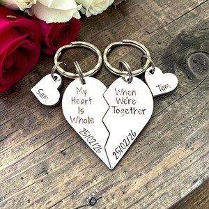 May include: Two silver-toned metal keychains shaped as a split heart. One piece is engraved with "My Heart Is Whole" and "25/02/26", the other with "When We're Together" and "25/02/26". Each keychain includes a small heart charm labelled "Sam" or "Tom".