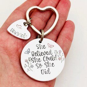 Pode incluir: Um porta-chaves de metal prateado com um anel em forma de cora&ccedil;&atilde;o, um pequeno pendente em forma de cora&ccedil;&atilde;o gravado com o nome Hannah e um &iacute;cone de cora&ccedil;&atilde;o, e um grande disco circular gravado com o texto She Believed She Could so she Did.