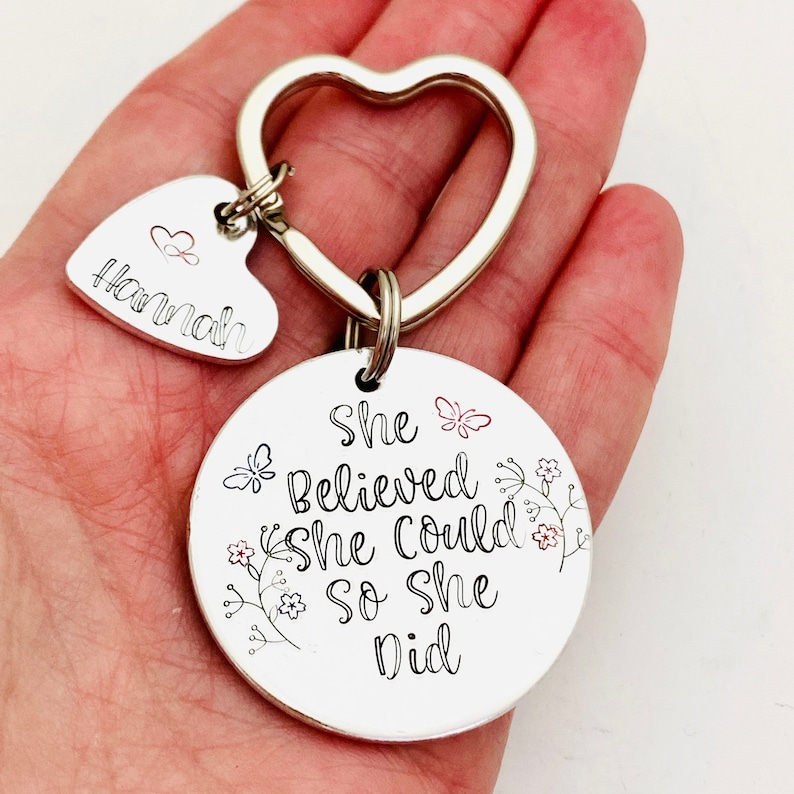 Pode incluir: Um porta-chaves de metal prateado com um anel em forma de cora&ccedil;&atilde;o, um pequeno pendente em forma de cora&ccedil;&atilde;o gravado com o nome Hannah e um &iacute;cone de cora&ccedil;&atilde;o, e um grande disco circular gravado com o texto She Believed She Could so she Did.