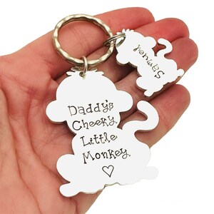 Puede incluir: Llavero de mono plateado con el texto "Daddy's Cheeky Little Monkey" y un coraz&oacute;n. Un peque&ntilde;o amuleto de mono est&aacute; unido al llavero.