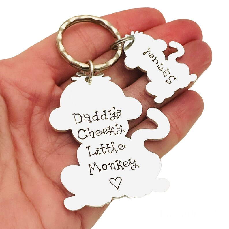Puede incluir: Llavero de mono plateado con el texto "Daddy's Cheeky Little Monkey" y un coraz&oacute;n. Un peque&ntilde;o amuleto de mono est&aacute; unido al llavero.