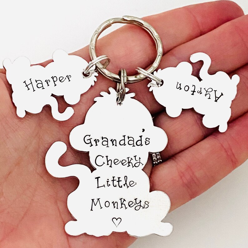 Puede incluir: Llavero de mono plateado con tres peque&ntilde;os dijes de mono. El dije de mono m&aacute;s grande tiene el texto "Grandad's Cheeky Little Monkeys" con un s&iacute;mbolo de coraz&oacute;n. Los dijes m&aacute;s peque&ntilde;os tienen los nombres "Harper", "Ava" y "Noah" grabados.