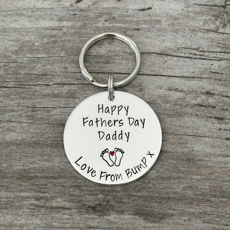 Peut inclure: Porte-cl&eacute;s argent&eacute; avec une &eacute;tiquette ronde qui dit "Joyeuse f&ecirc;te des p&egrave;res Papa Amour de Bump" avec un c&oelig;ur rouge et deux empreintes de pas.